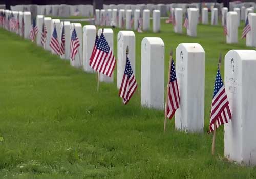 Image of American flags flying near soldiers' headstones.